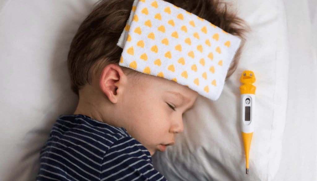 Sleeping toddler with a cool compress and thermometer, recovering from illness in a cozy setting.